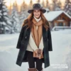 Retrato de una mujer sonriente de pie en un paisaje nevado con una cabaña de madera en el fondo. Viste un abrigo largo de cuadros escoceses en tonos verde botella y azul marino, un suéter de cuello alto color crema, una bufanda camel de punto y un sombrero de fieltro gris oscuro con un adorno floral/escarchado.